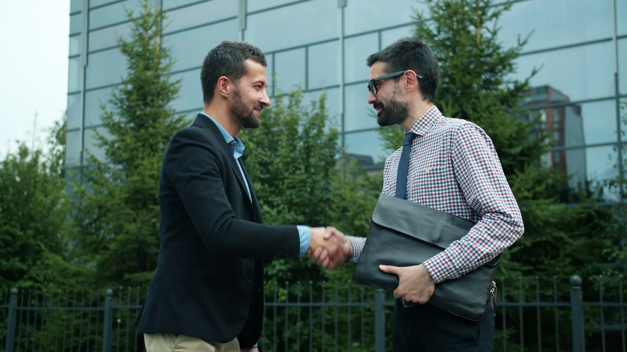 Two men shaking hands outdoors in front of trees