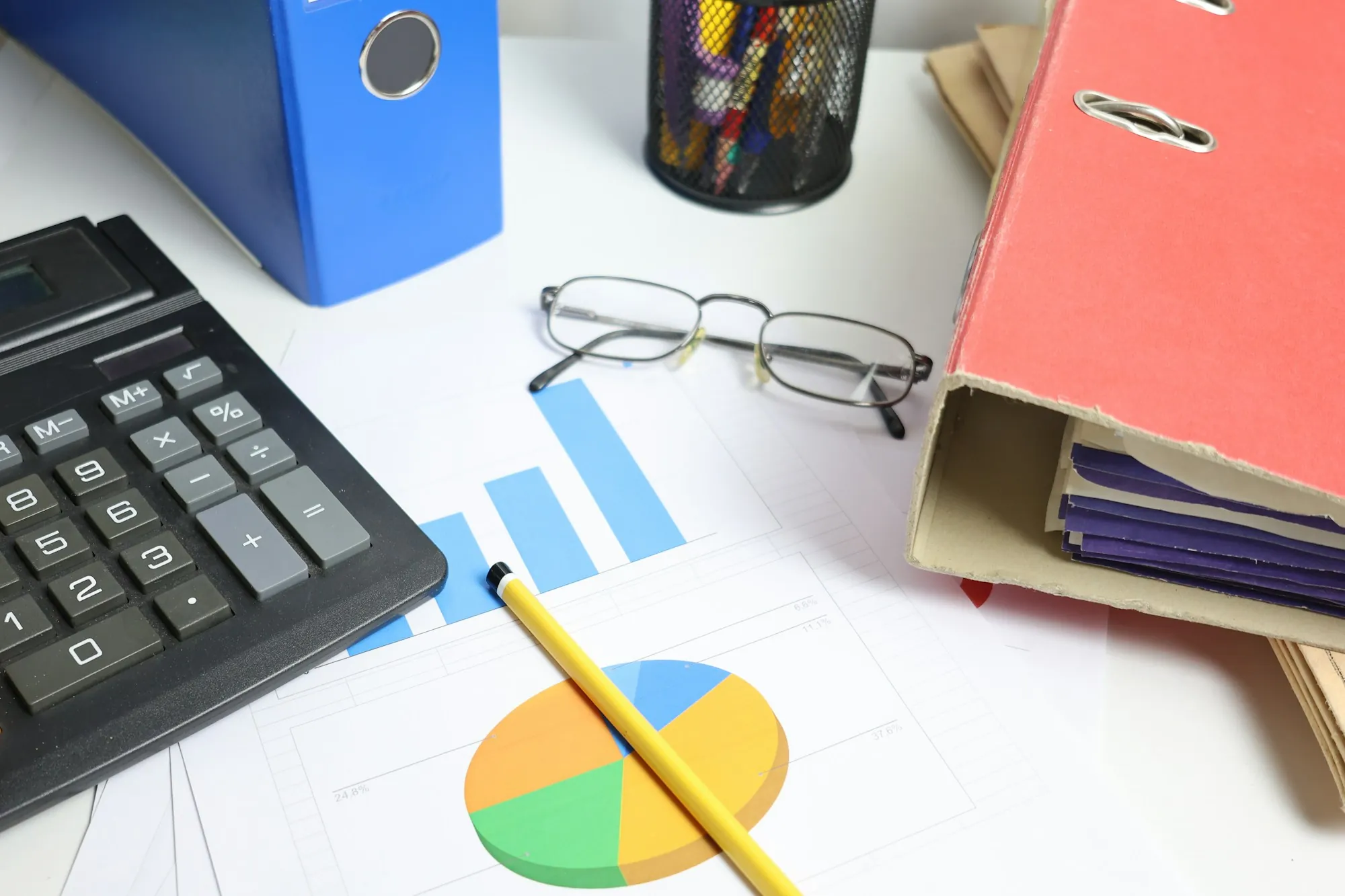 Calculator beside a pie chart, glasses and a binder