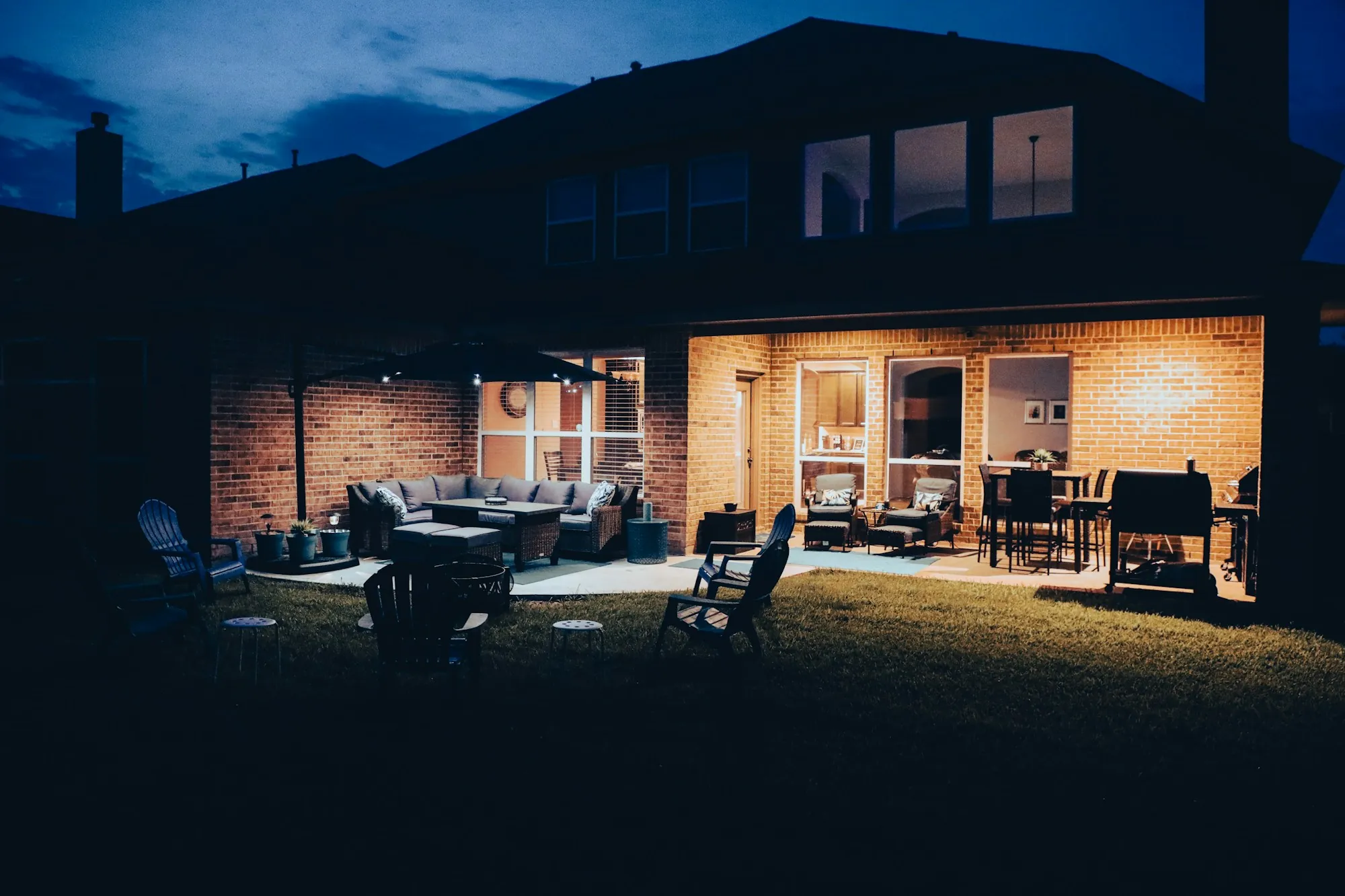 Back patio of a brick house lit up in the evening with outdoor seating